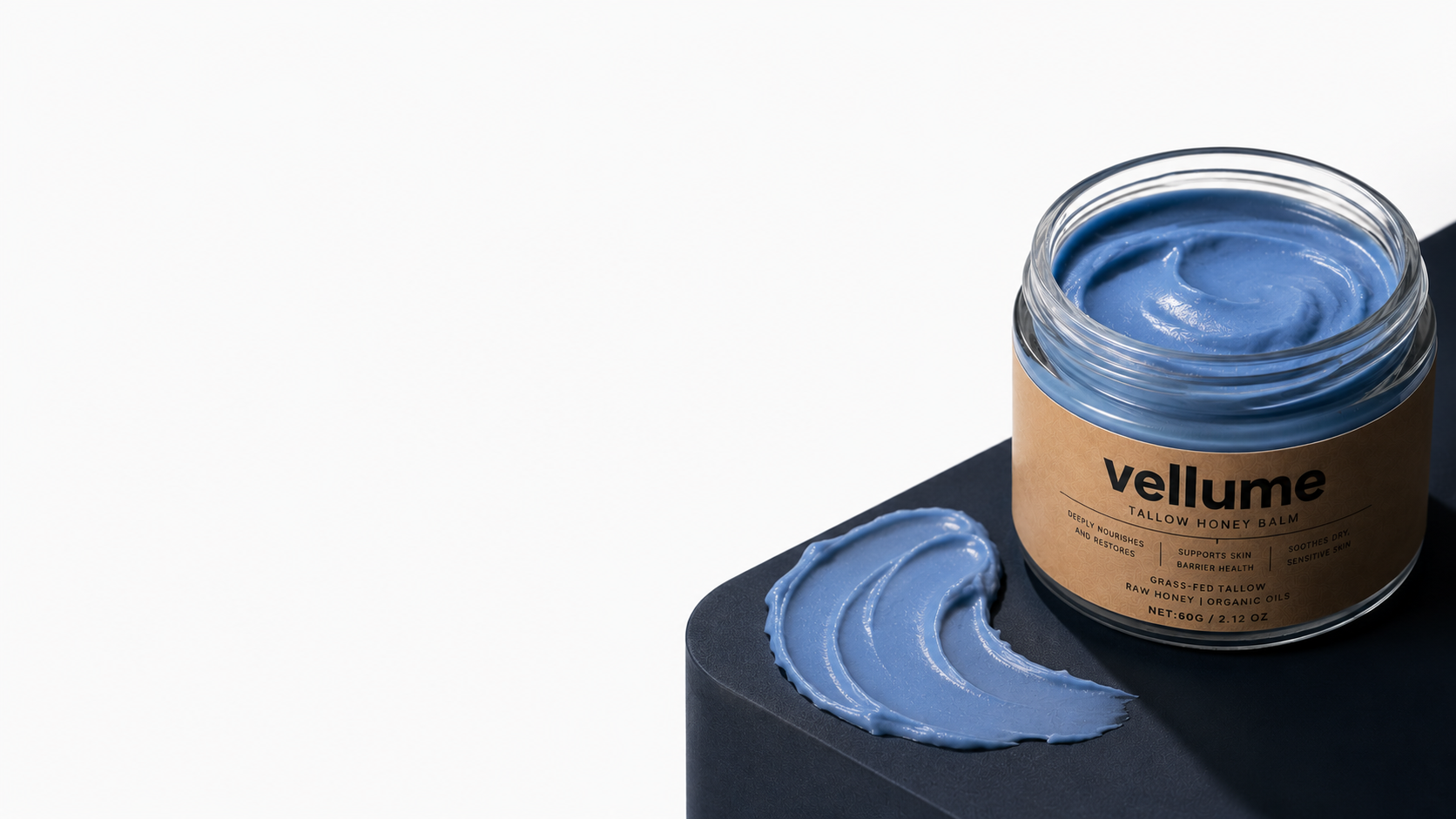 Vellume Tallow Honey Balm kraft jar on a concrete plinth with a periwinkle balm smear, beside a clean off-white wall